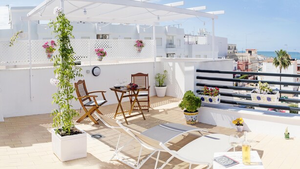 Une terrasse sur le toit, agrémentée d’une pergola blanche, de deux chaises en bois, d’une table avec un plateau en verre et de plantes en pot.