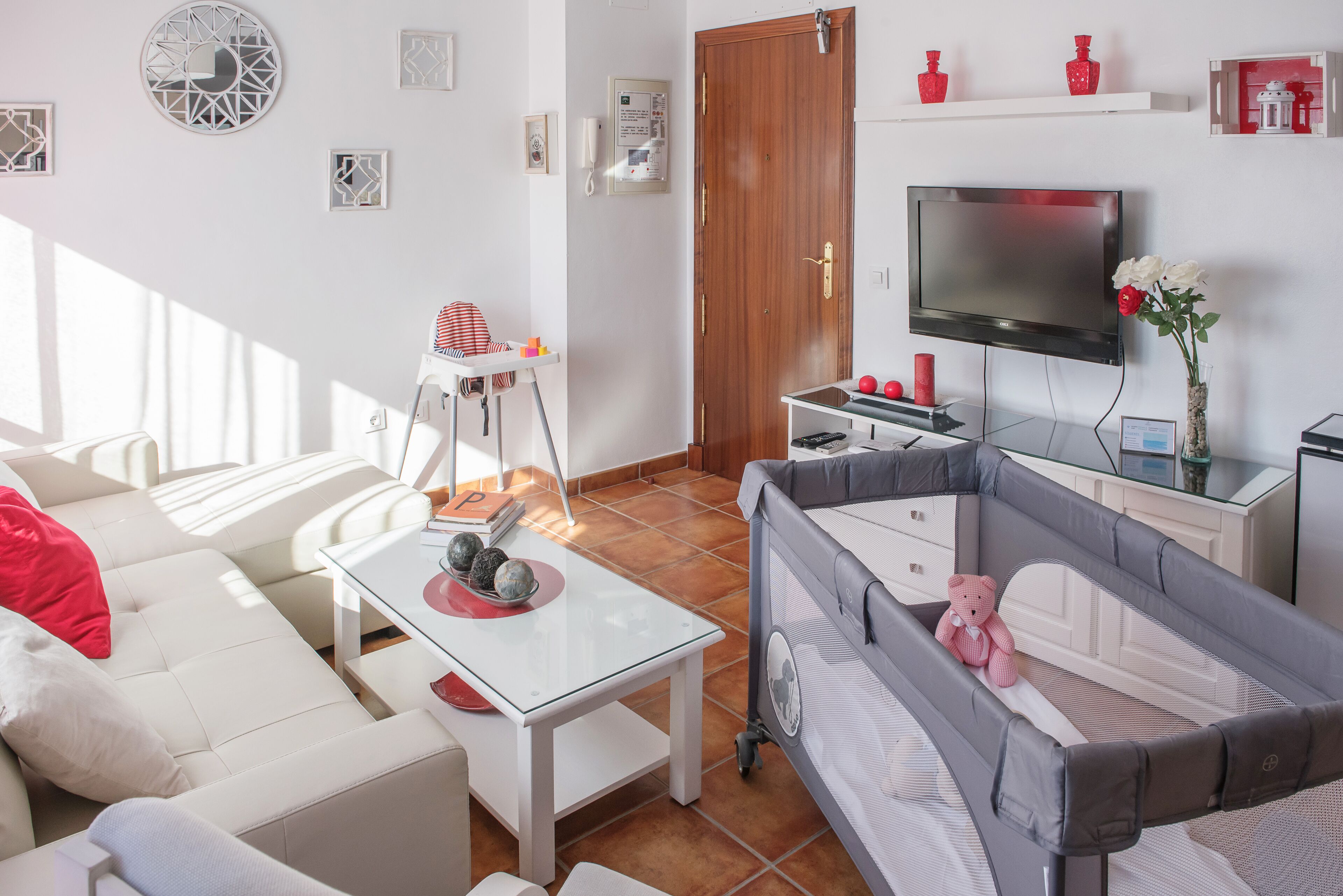 Una sala de estar con sofá, mesa de centro, televisor y corralito para bebé.