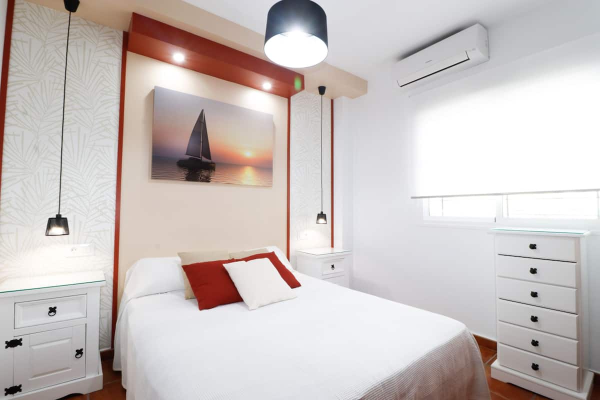 Een slaapkamer met een bed, nachtkastjes, een dressoir en een schilderij van een zeilboot aan de muur.