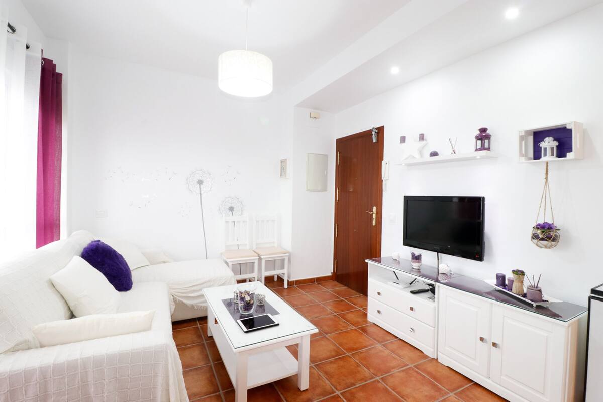 Een moderne woonkamer met een witte bank, een glazen salontafel, een flatscreen televisie en een witte kast.