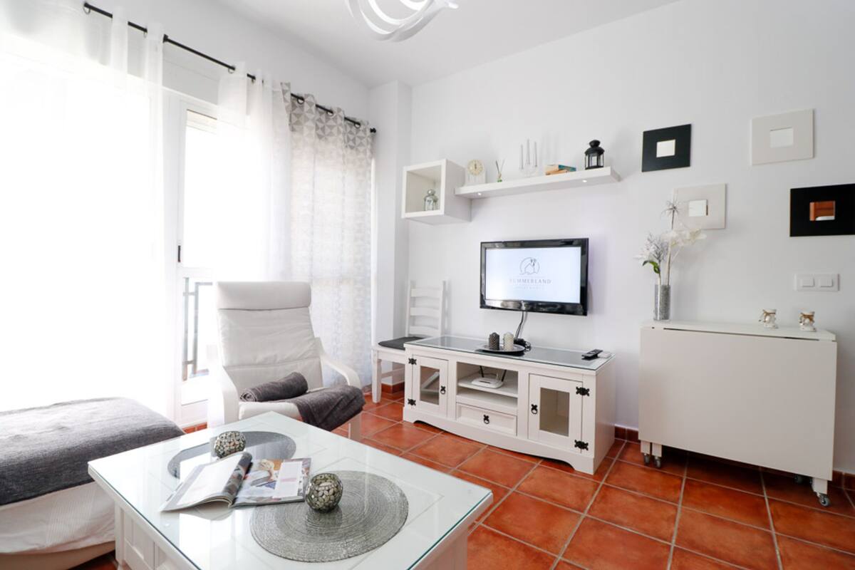 Een moderne woonkamer met een televisie, witte meubels en een betegelde vloer.