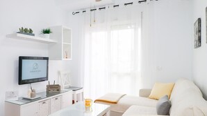 Un salon moderne avec un téléviseur à écran plat, une table basse en verre, un canapé blanc et un meuble blanc.