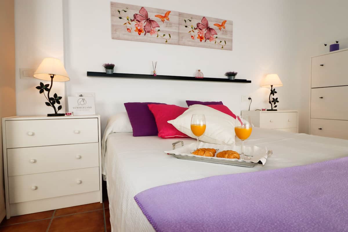 Een keurig opgemaakt slaapkamer met een bed, kussens, nachtkastjes en een dienblad met croissants en sinaasappelsap.