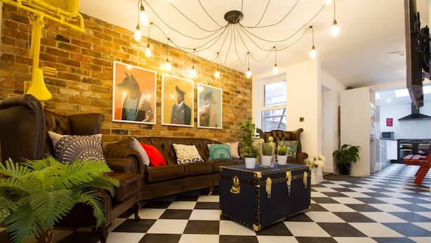 A living room with a checkered floor, a leather sofa, a vintage trunk, and framed artwork on the wall. - Modern Design House (Liverpool)
