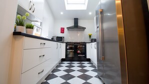 A modern kitchen with white cabinets, a black and white checkered floor, a stainless steel refrigerator, and an oven. - Modern Design House (Liverpool)