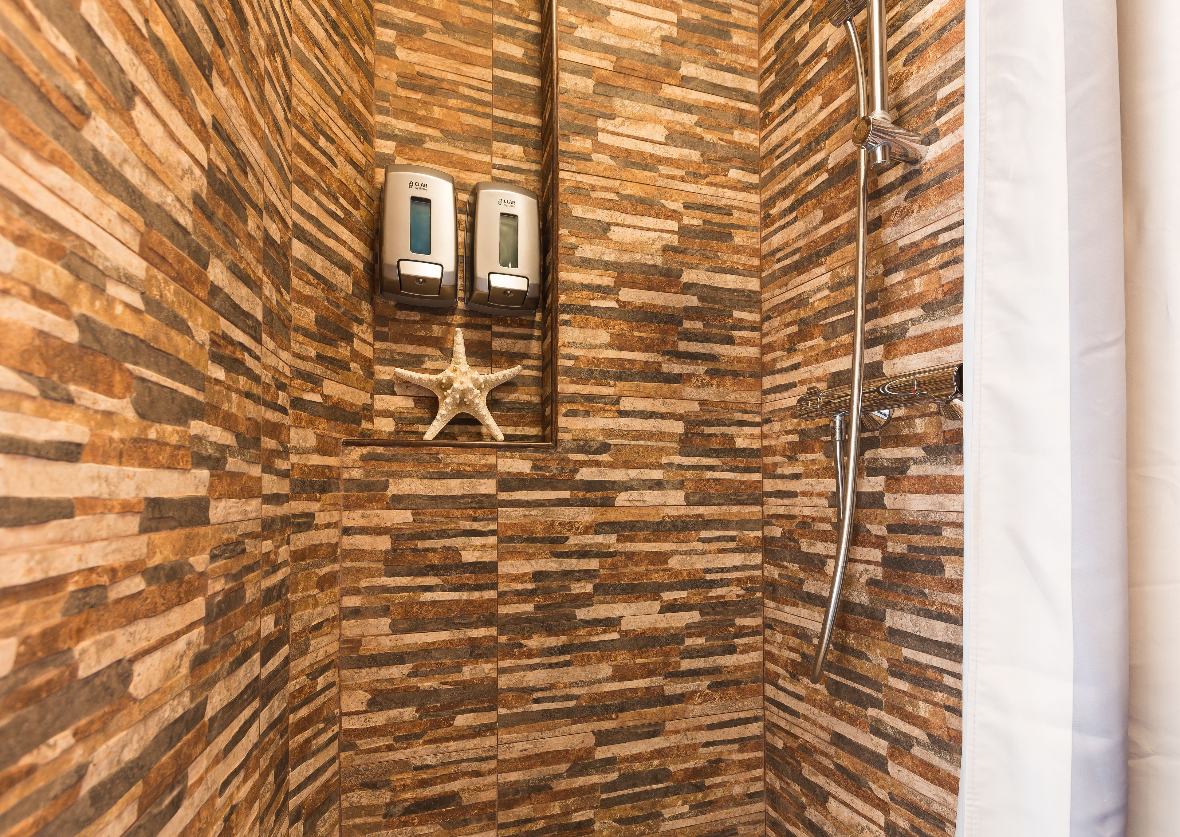 Una ducha con pared de piedra, una decoración de estrella de mar y dos secadores de manos.