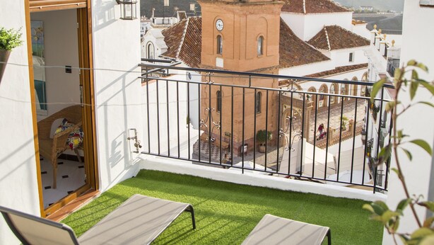 Un balcón con césped artificial, dos sillones de descanso y vistas a una torre de iglesia.
