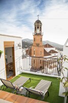 Un balcón con césped artificial, dos sillones de descanso y vistas a una torre de iglesia.