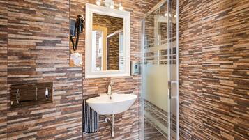 Un baño moderno con pared de diseño tipo piedra, un lavabo blanco y una cabina de ducha de vidrio.
