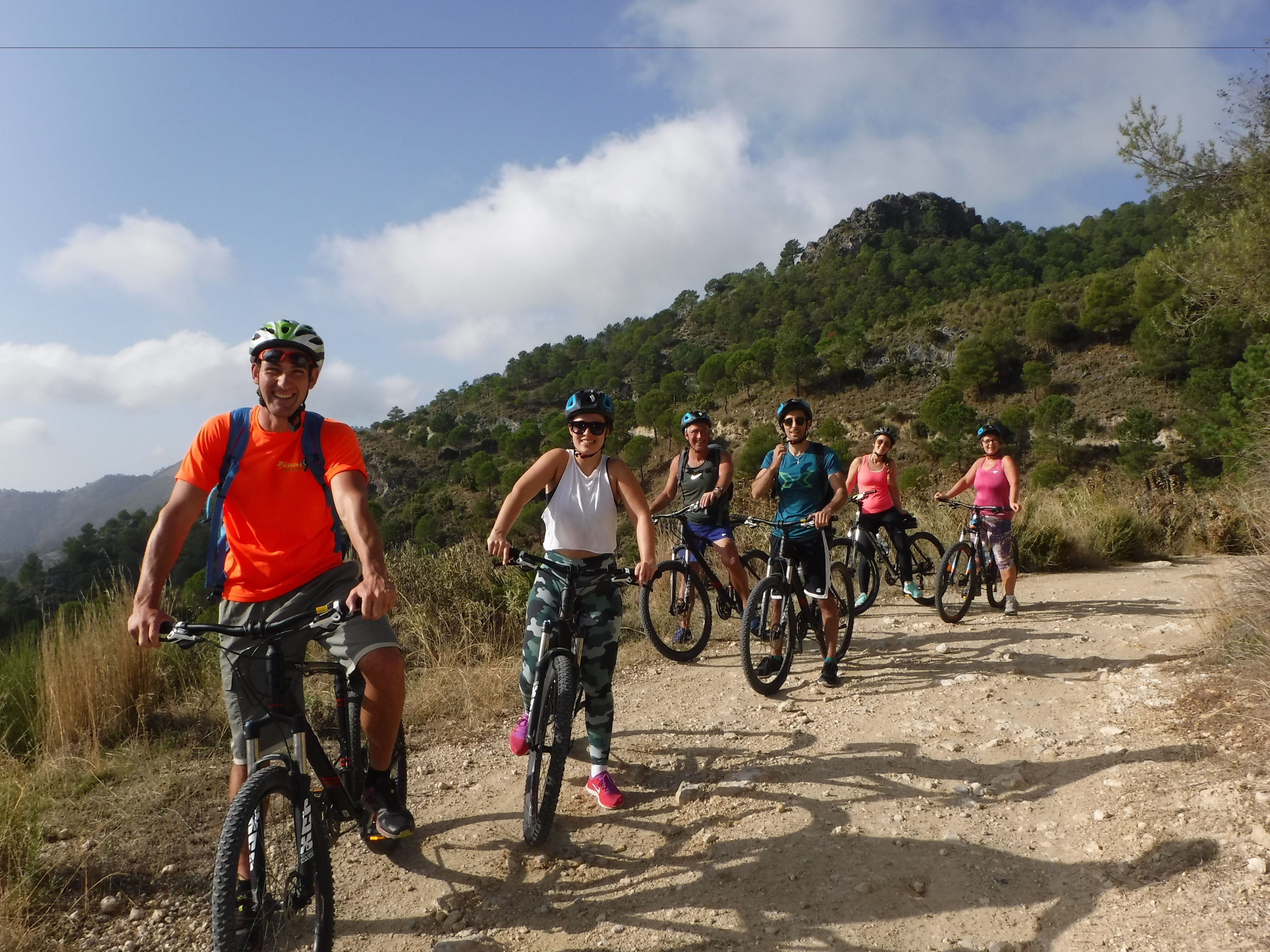 Un grup de persones a un camí de terra amb bicicletes, envoltat de vegetació i turons.