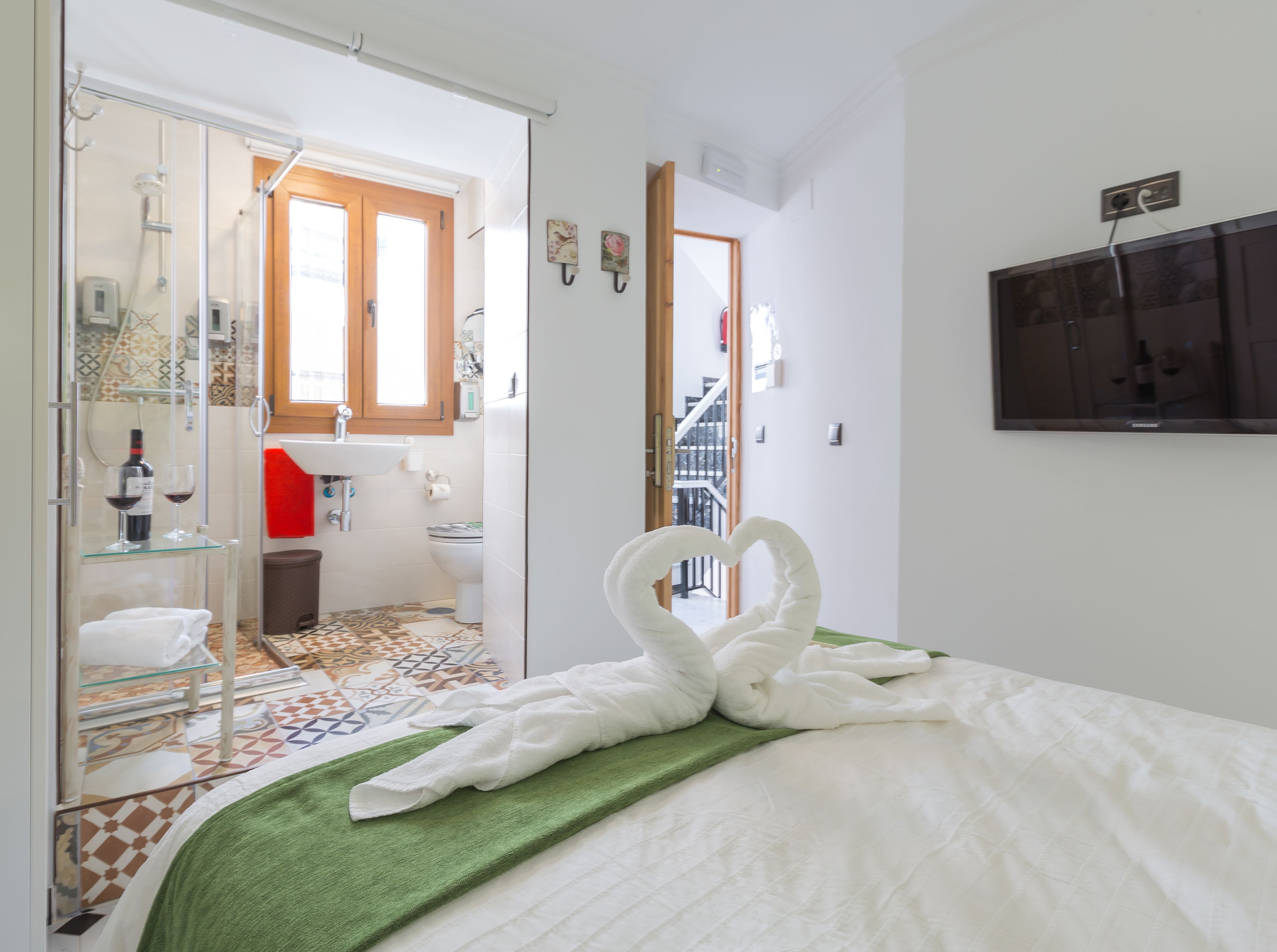 A hotel room with a bed, a green towel, a glass shower enclosure, a sink, and a toilet.