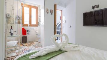 A hotel room with a bed, a green towel, a glass shower enclosure, a sink, and a toilet.