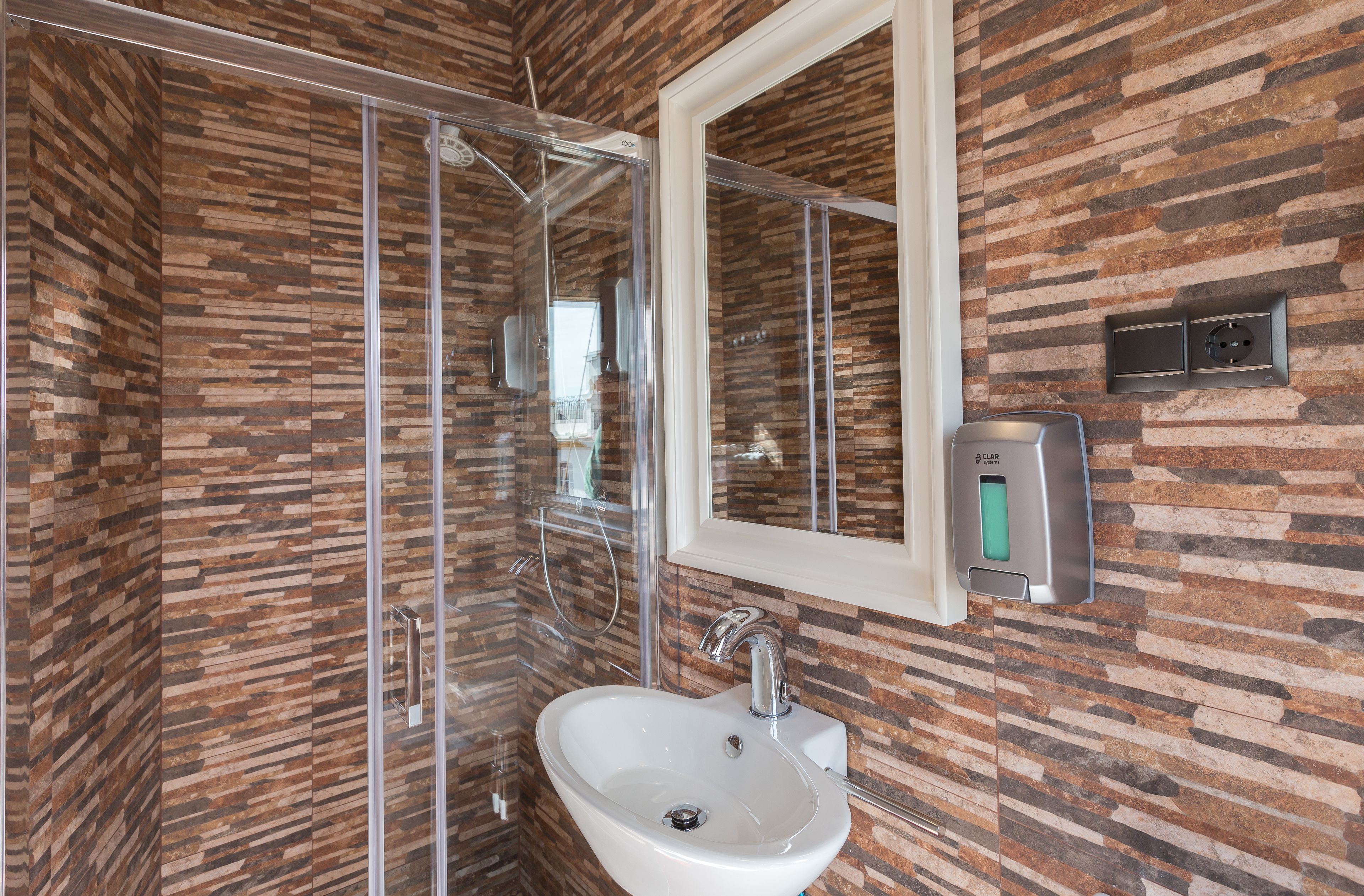 Un baño moderno con pared de estilo piedra, cabina de ducha de vidrio, lavabo blanco y un espejo.