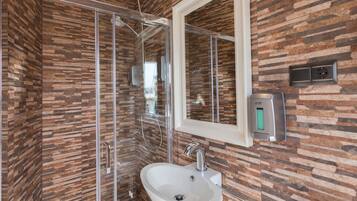 Un baño moderno con pared de estilo piedra, cabina de ducha de vidrio, lavabo blanco y un espejo.