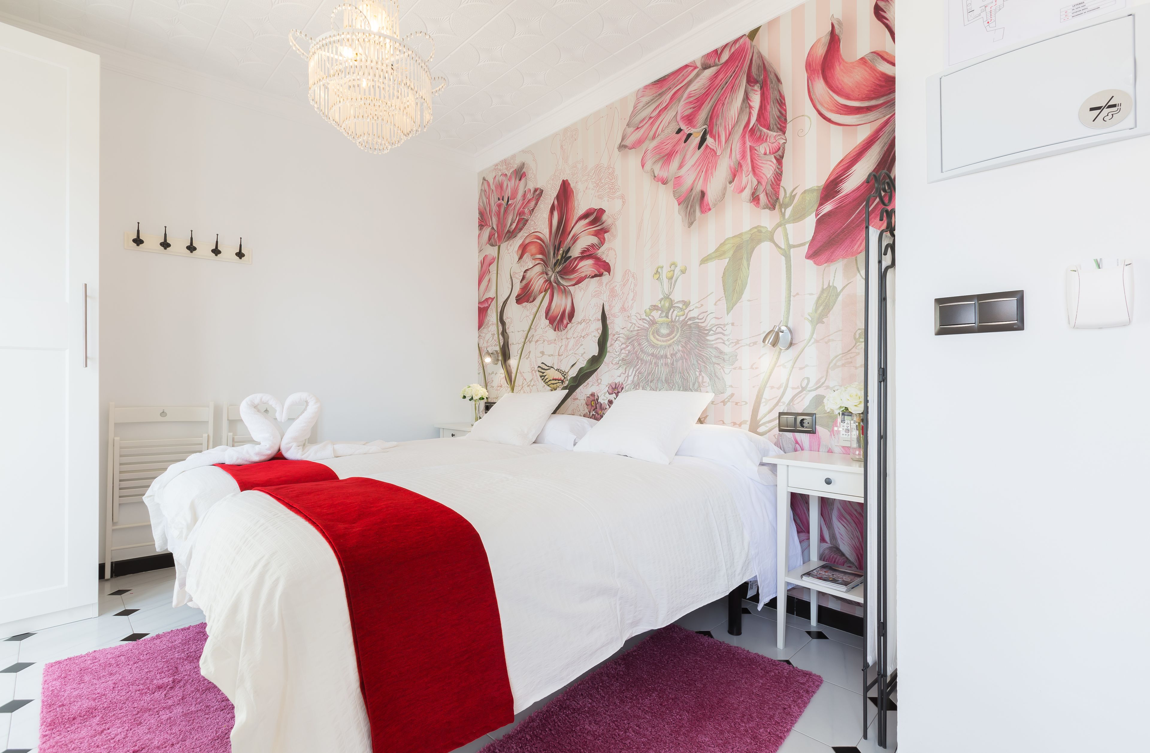 Une chambre bien rangée, avec un grand lit, un bureau et un mur recouvert d’un papier peint à motifs floraux.