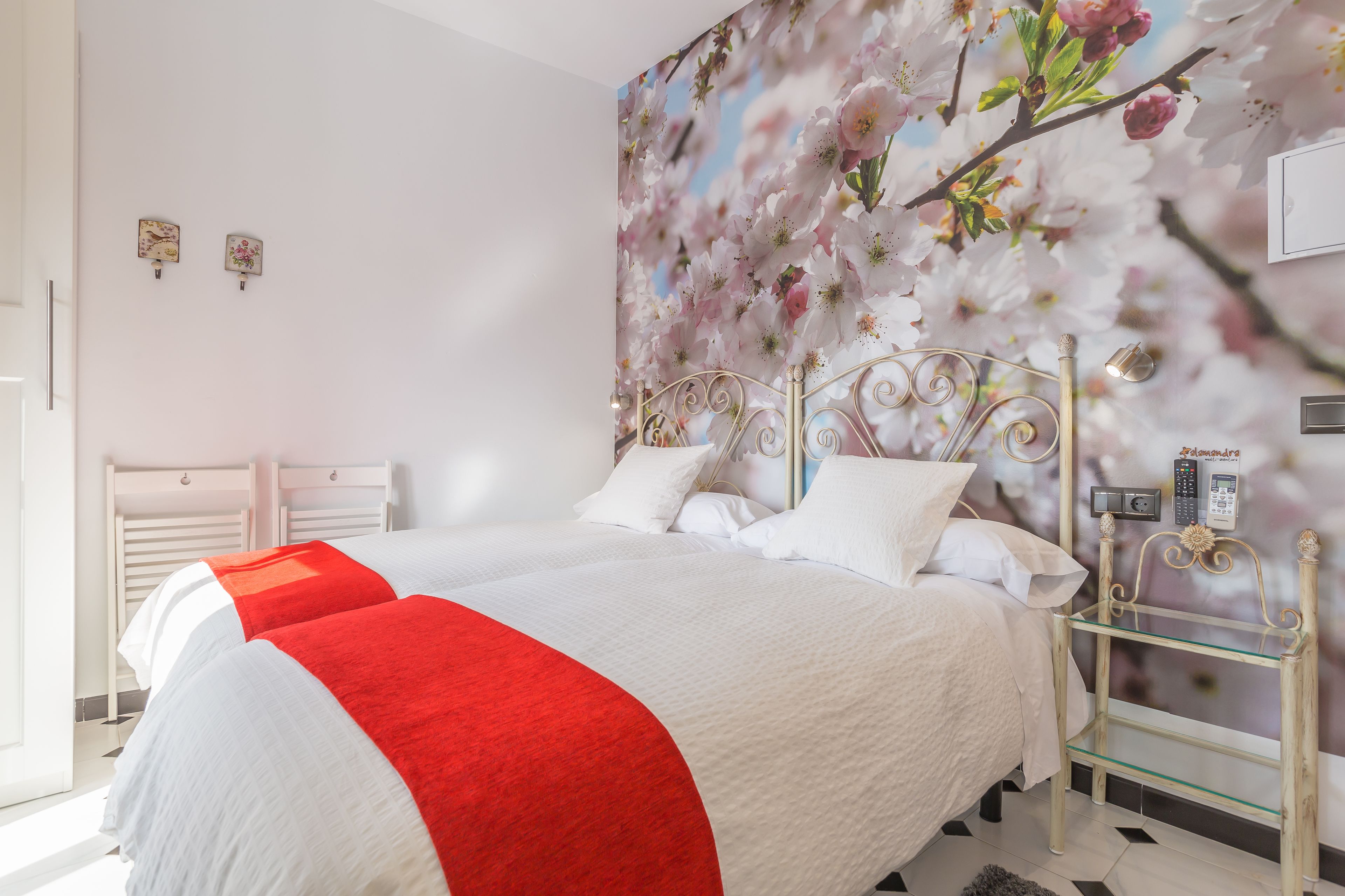 A bedroom with a bed, a bedside table, and a wall-mounted alarm clock.