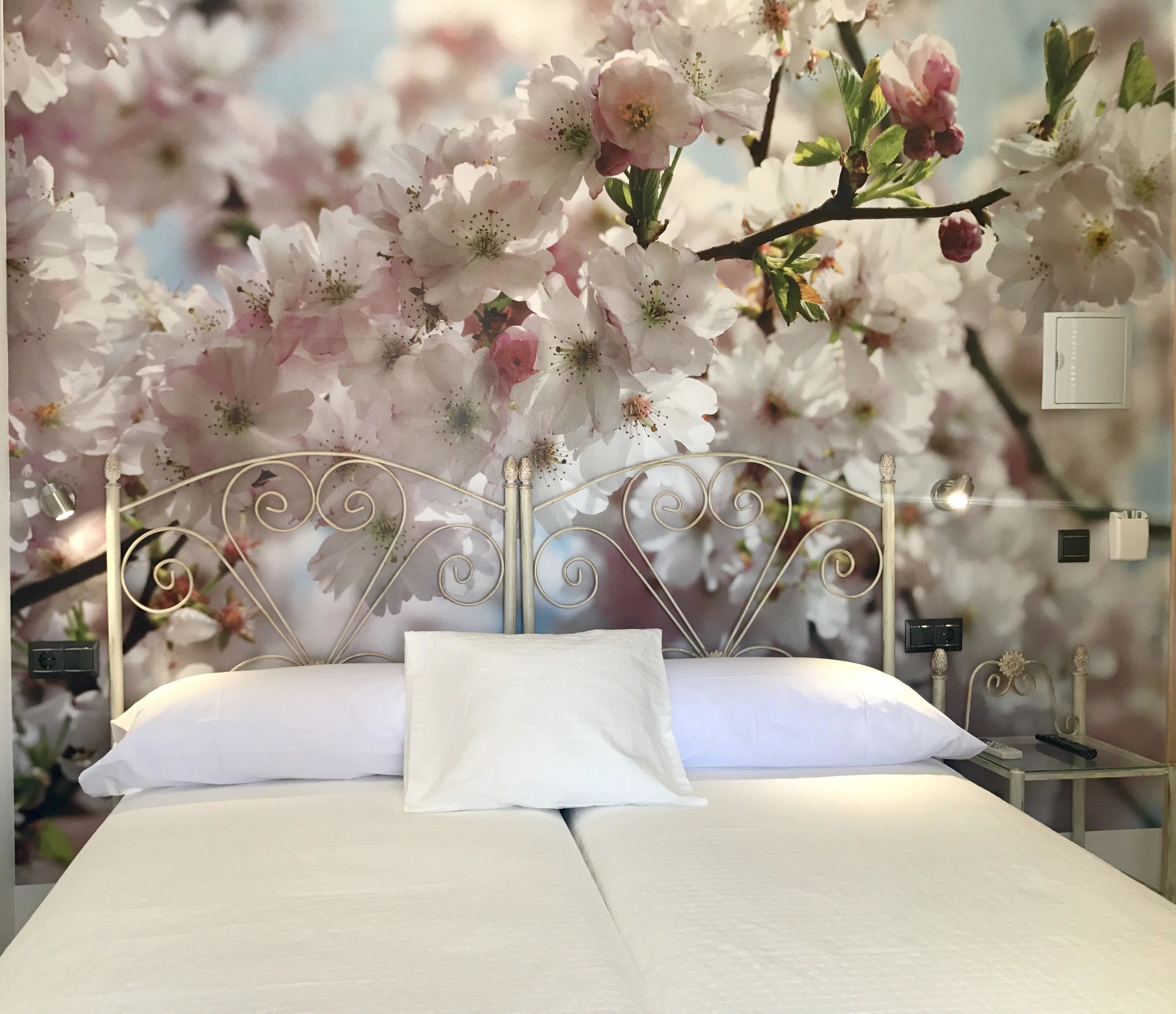 A bed with white linens and a metal headboard, set against a backdrop of cherry blossoms.
