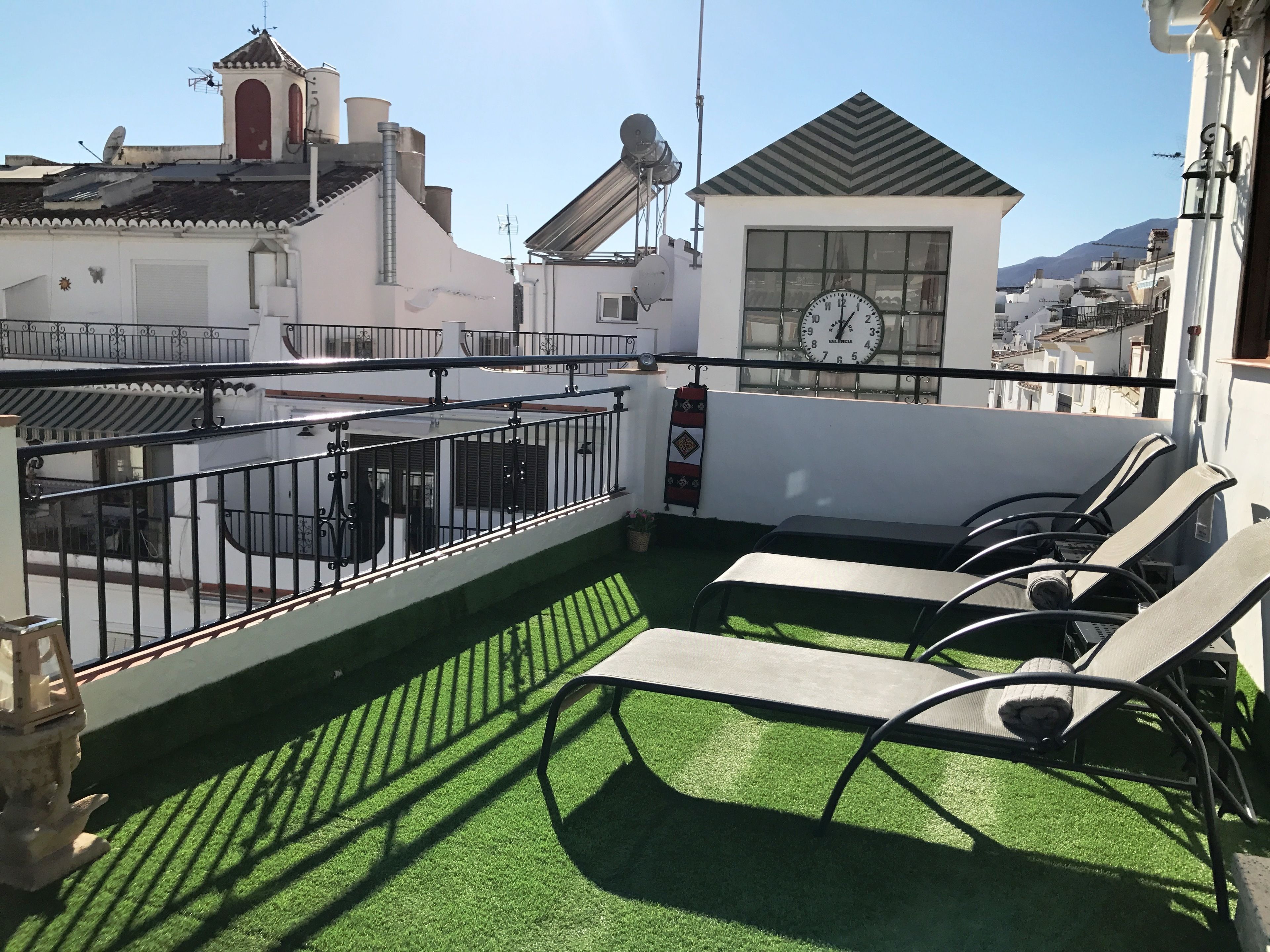 Une terrasse sur le toit avec du gazon synthétique, des sièges d’extérieur et une horloge.