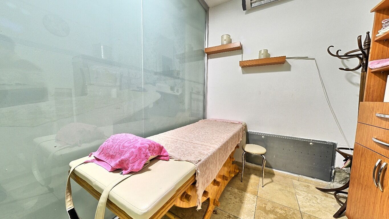 A small room with a single bed, a small stool, a cabinet, and a wall-mounted shelf.