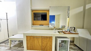 A compact hotel room with a kitchenette, a small refrigerator, a wooden cabinet, a flat-screen TV mounted on the wall, and a window with a view of the night sky. - Corum Buyuk Otel (Corum)