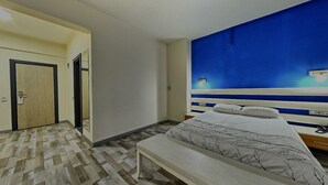 A bedroom with a bed, a bench, a nightstand, a wall-mounted TV, and a door. - Corum Buyuk Otel (Corum)