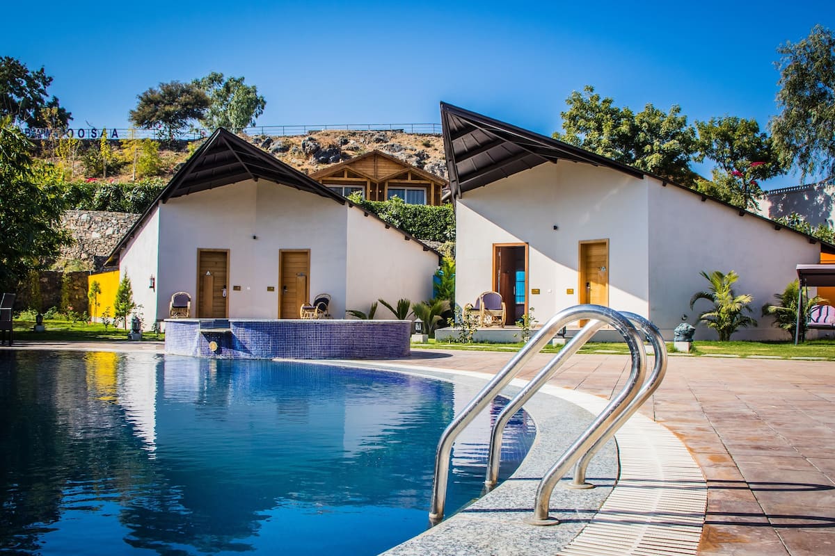 A pool area with two white buildings, each with a door and window, and a clear blue sky.