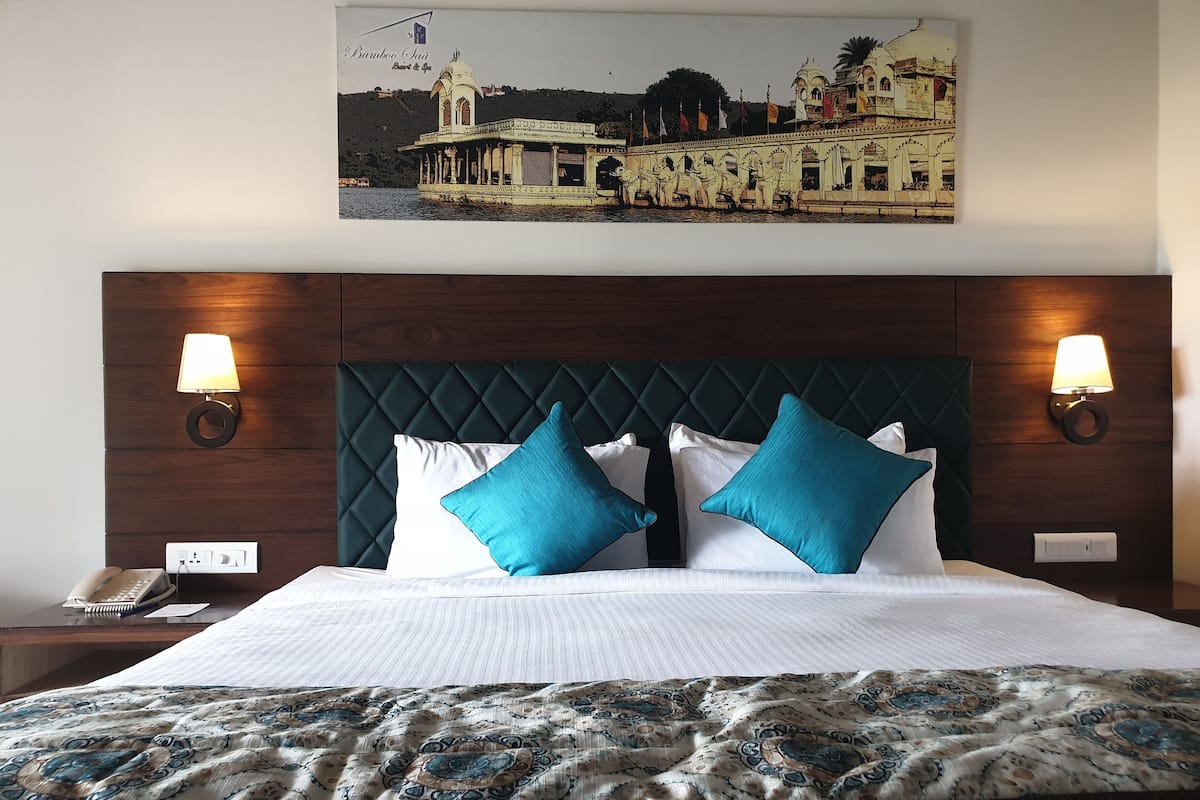 A hotel room with a large bed, two wall-mounted lamps, a telephone, and a framed picture of a building on the wall.