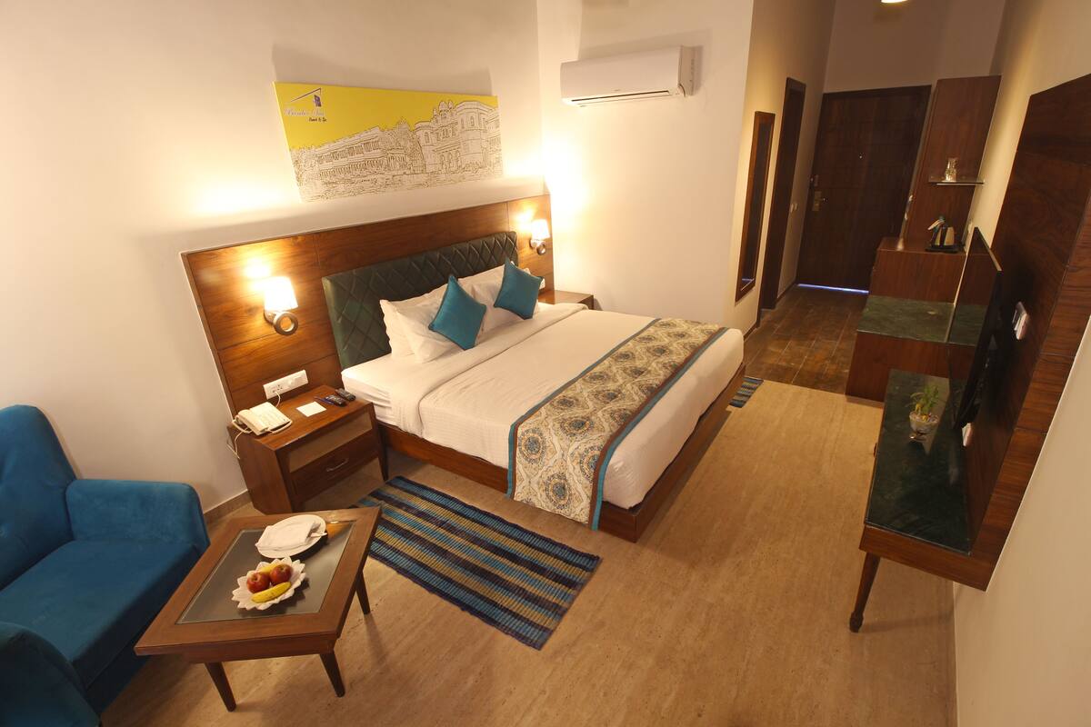 A hotel room with a bed, bedside table, lamp, and a blue armchair.
