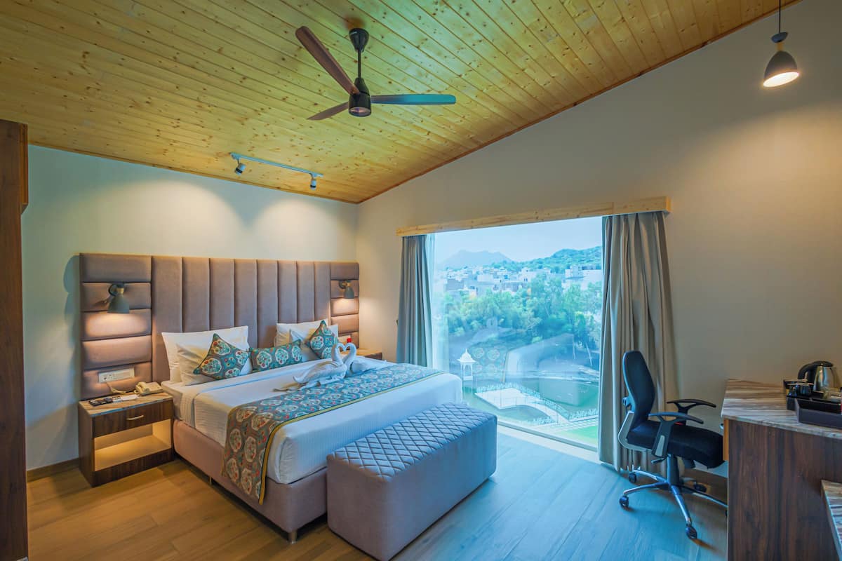 A bedroom with a large bed, a desk, and a view of a cityscape through the window.