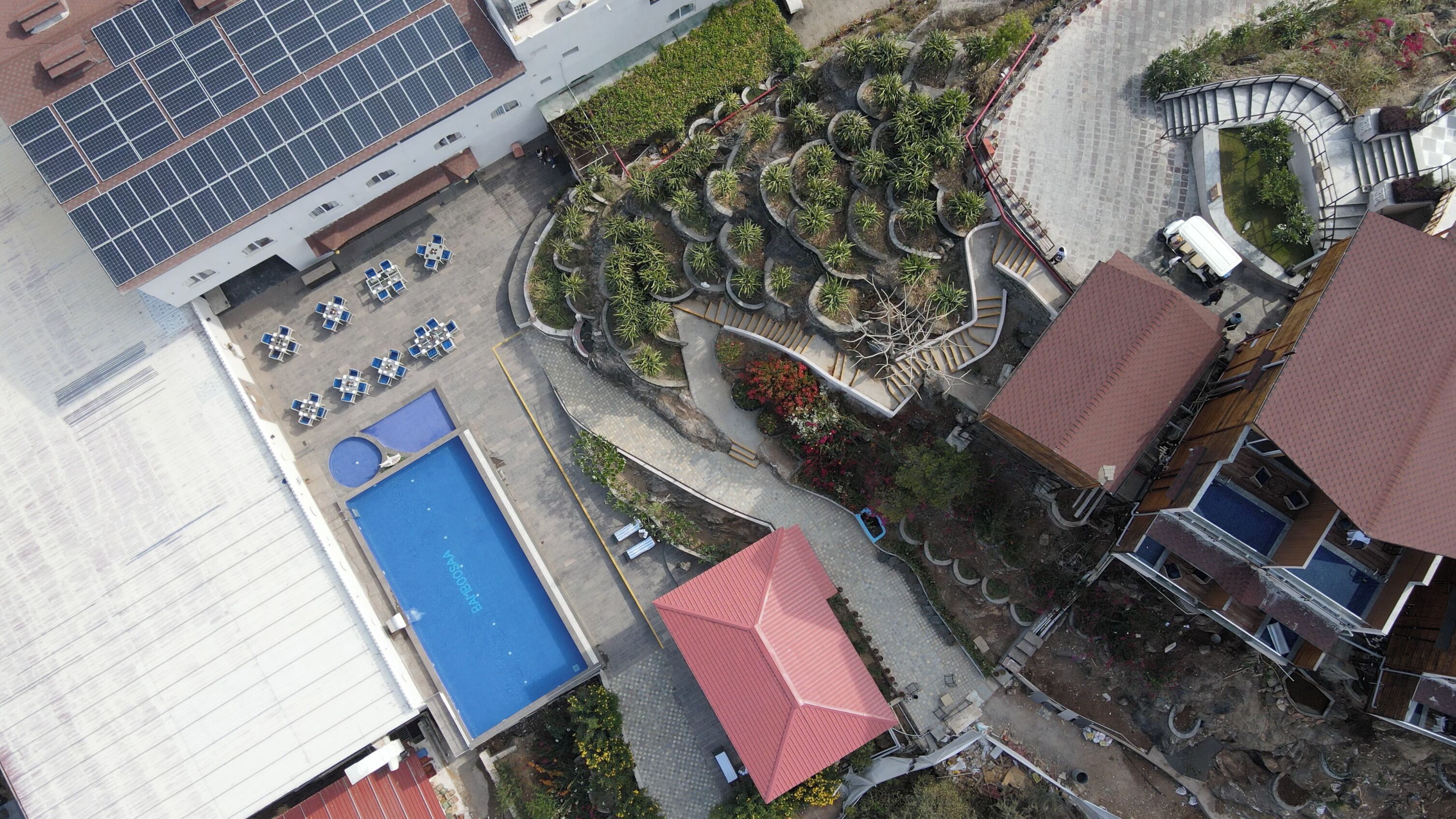 Eine Vogelperspektive eines Hotels mit Schwimmbad, Solaranlage und angelegtem Garten.