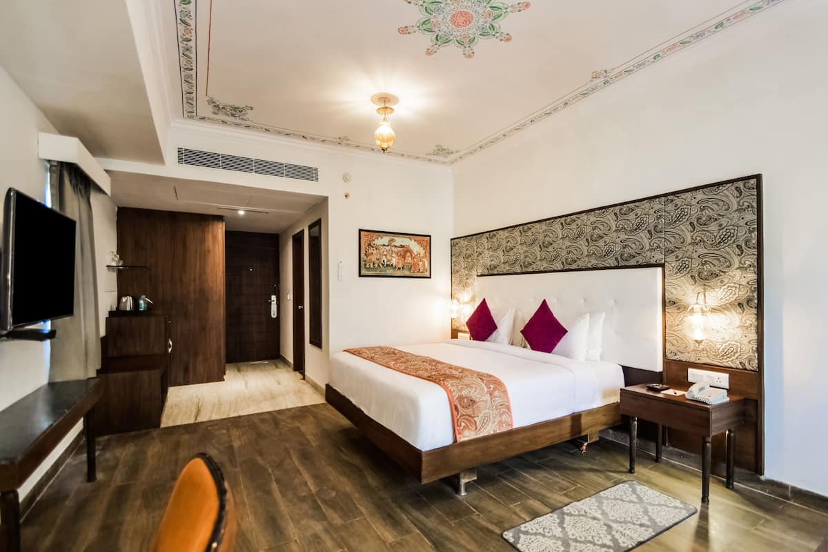 A hotel room with a bed, a desk, a chair, a television, and a decorative ceiling.