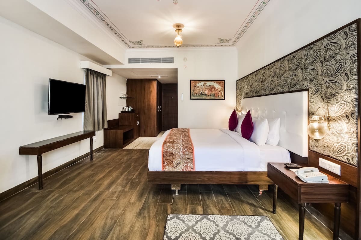A hotel room with a large bed, a TV, a desk, and a patterned wall.
