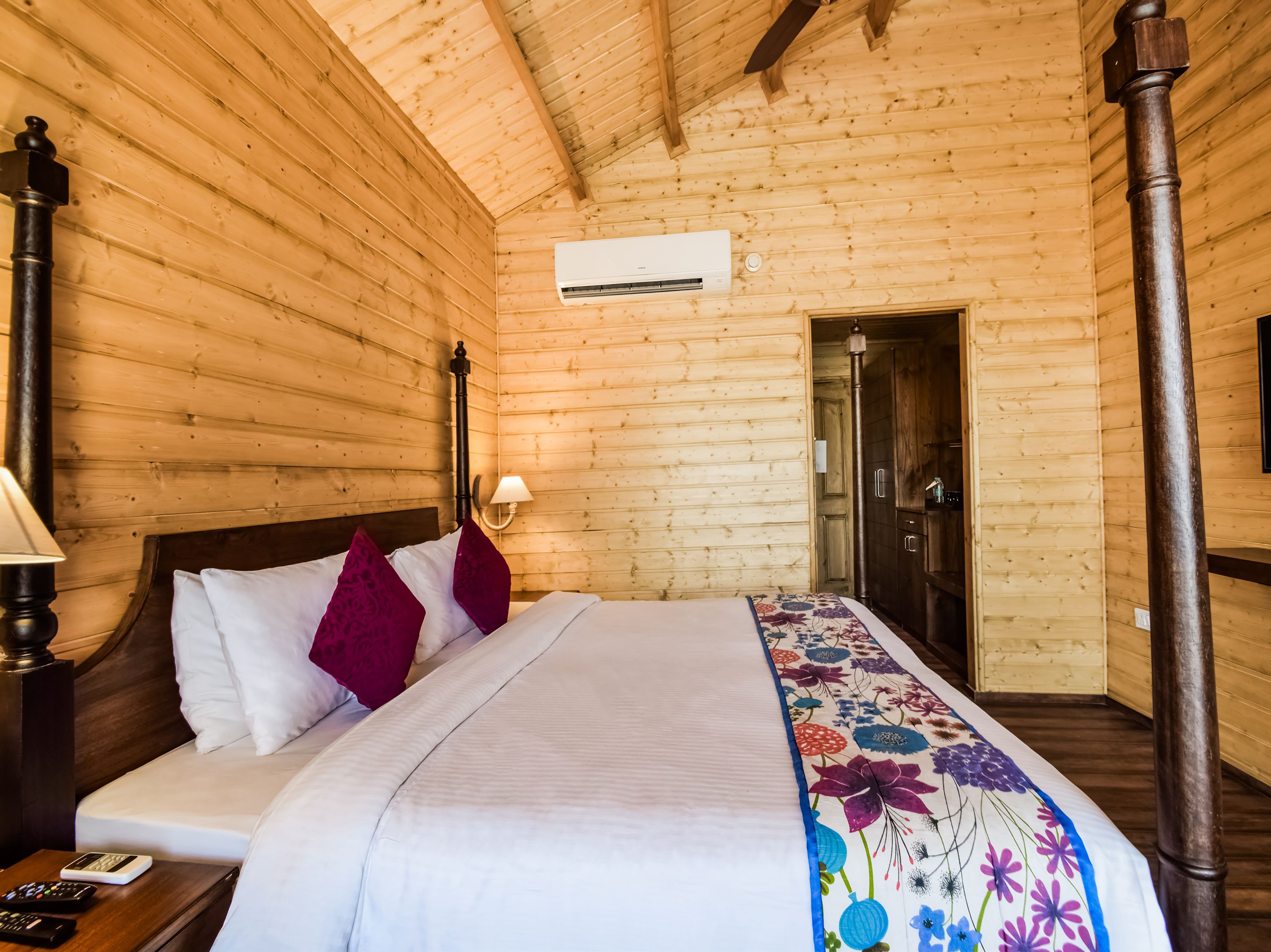 A wooden cabin-style bedroom with a bed, a nightstand, a lamp, and a door.