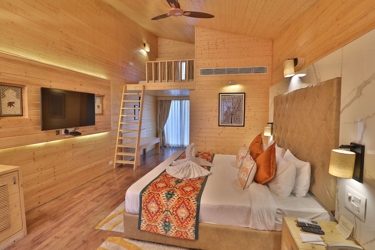 A wooden cabin-style room with a loft bed, a TV mounted on the wall, and a ladder leading to the loft.