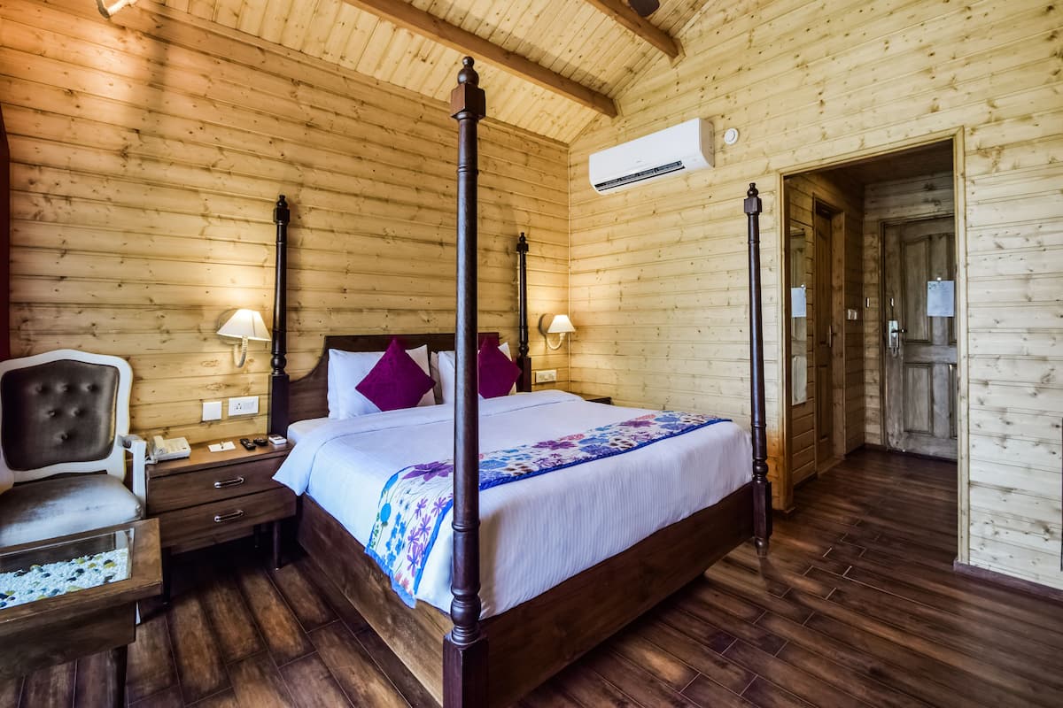 A four-poster bed with a wooden headboard, two bedside tables with lamps, a nightstand, and a wooden floor.