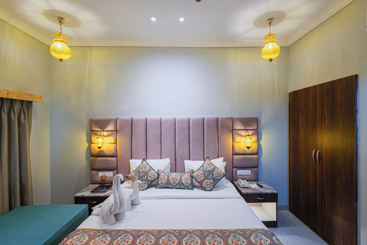 A hotel room with a large bed, two bedside tables, a wardrobe, and pendant lights.