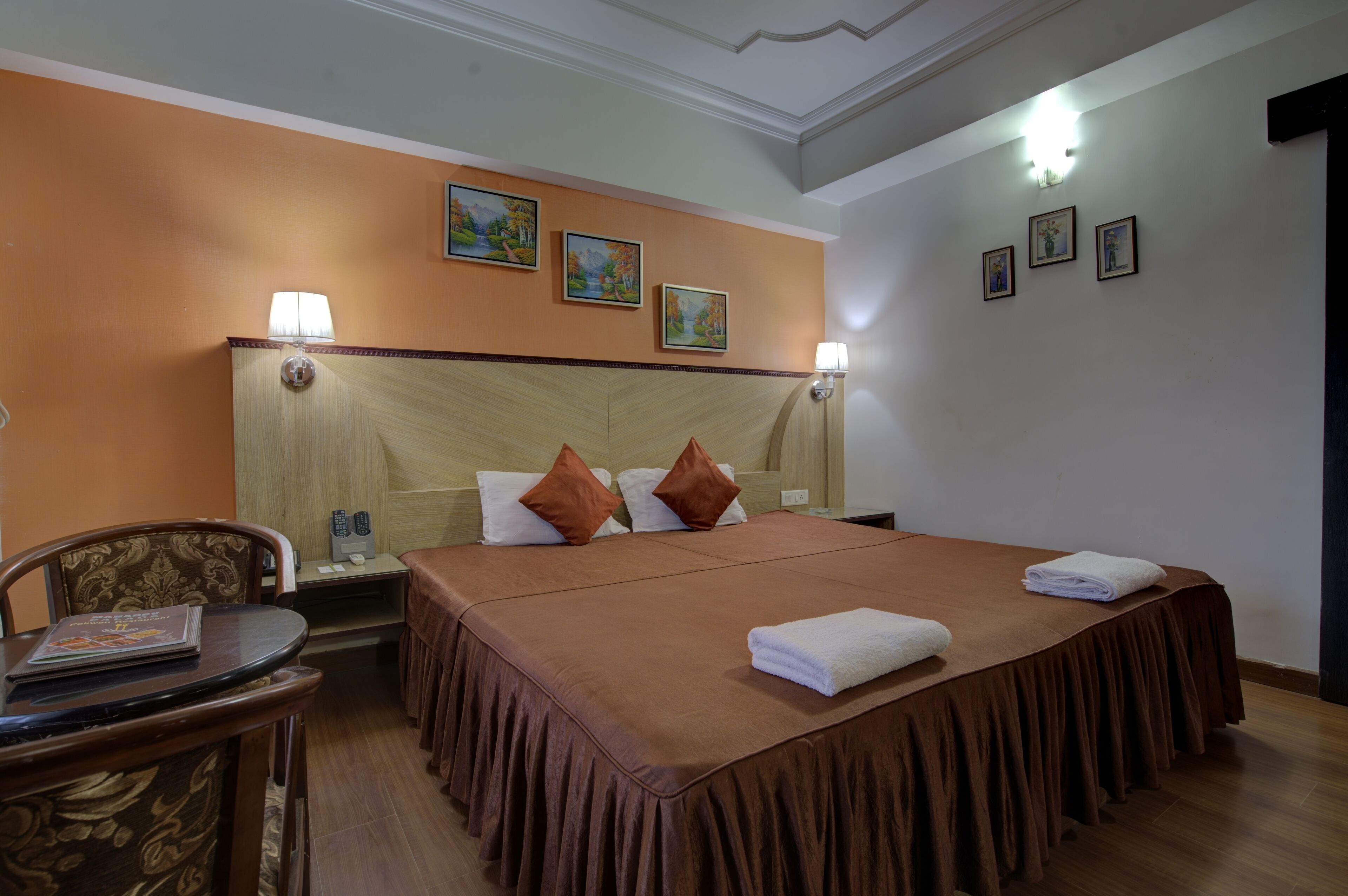 A hotel room with a large bed, two pillows, a nightstand, a lamp, and a chair.