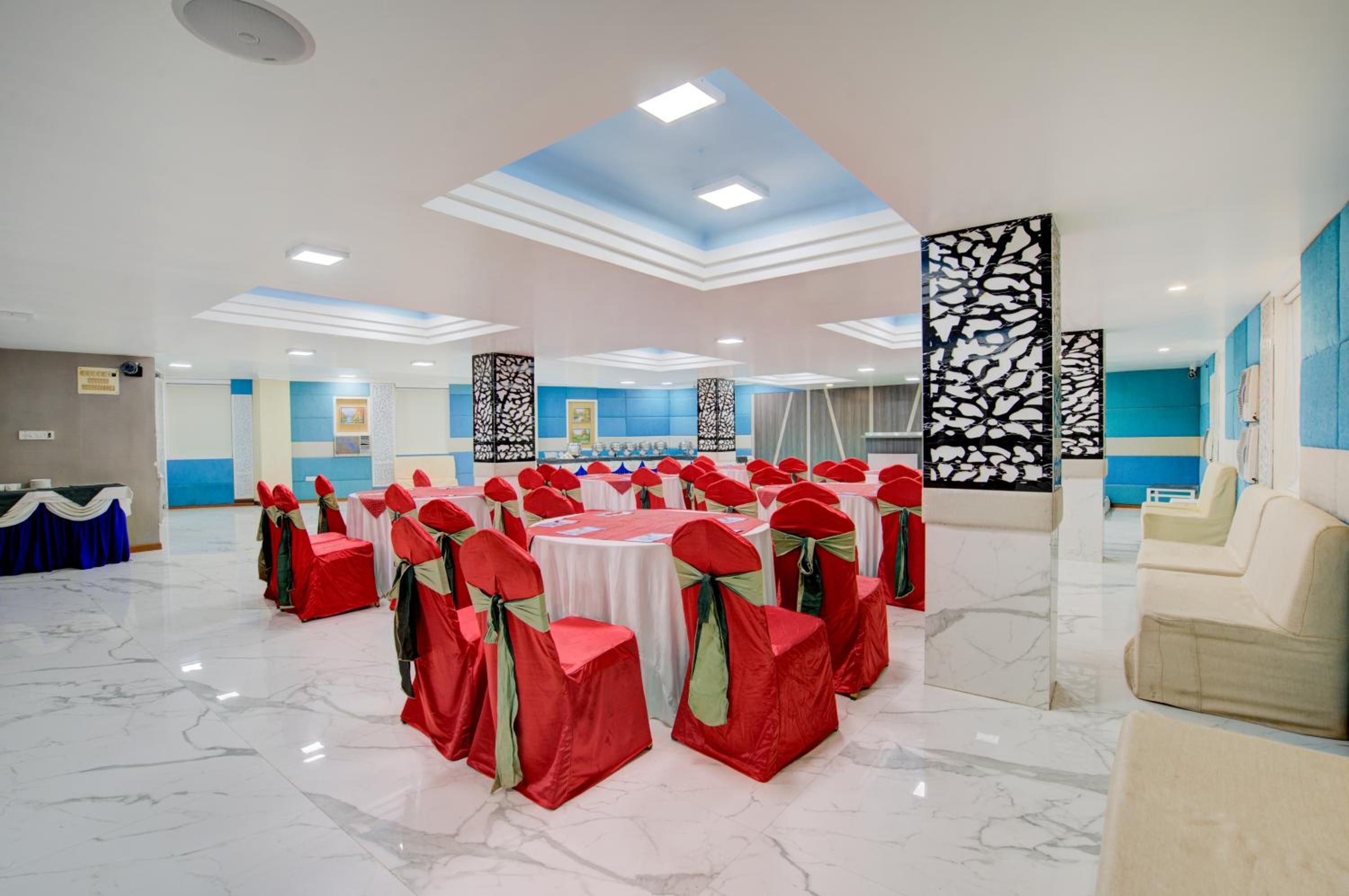 Un salón de banquetes con mesas redondas, sillas rojas y blancas, y una decoración azul y blanca.