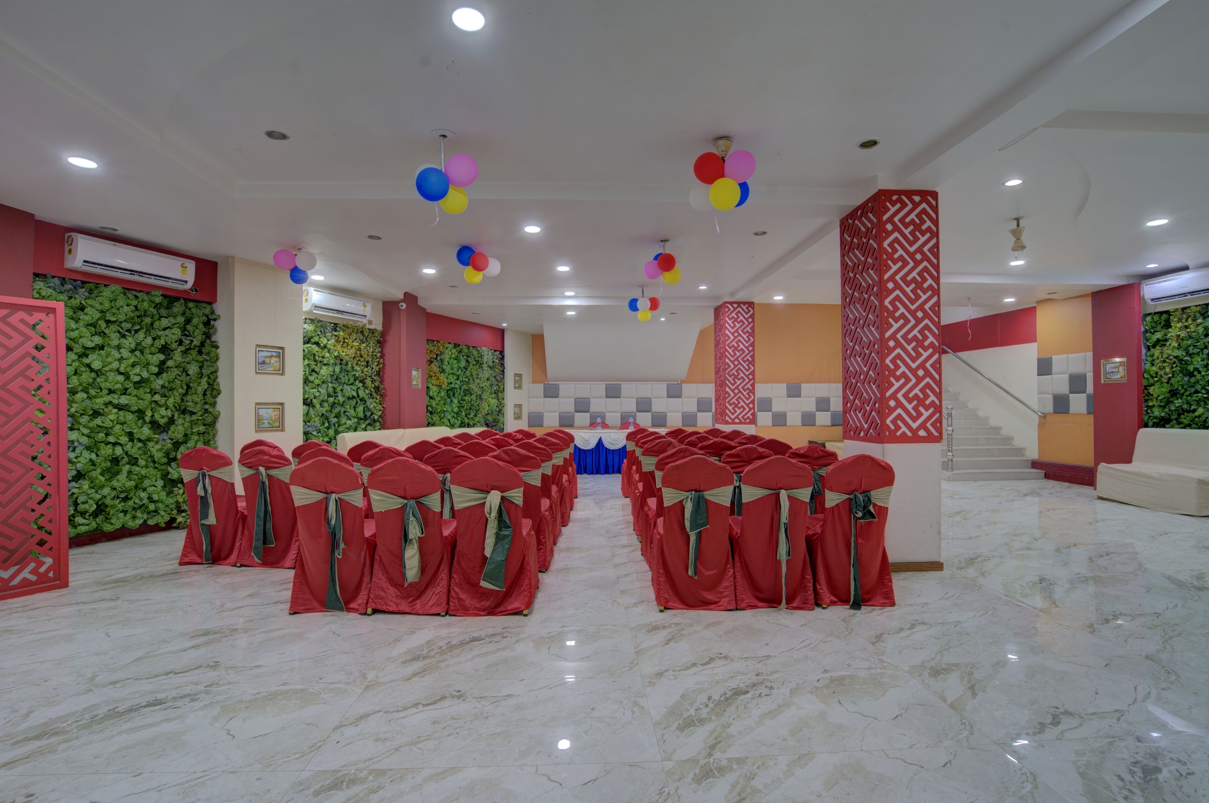 A spacious hall with rows of red chairs, a stage with a blue curtain, and a staircase with a patterned wall.