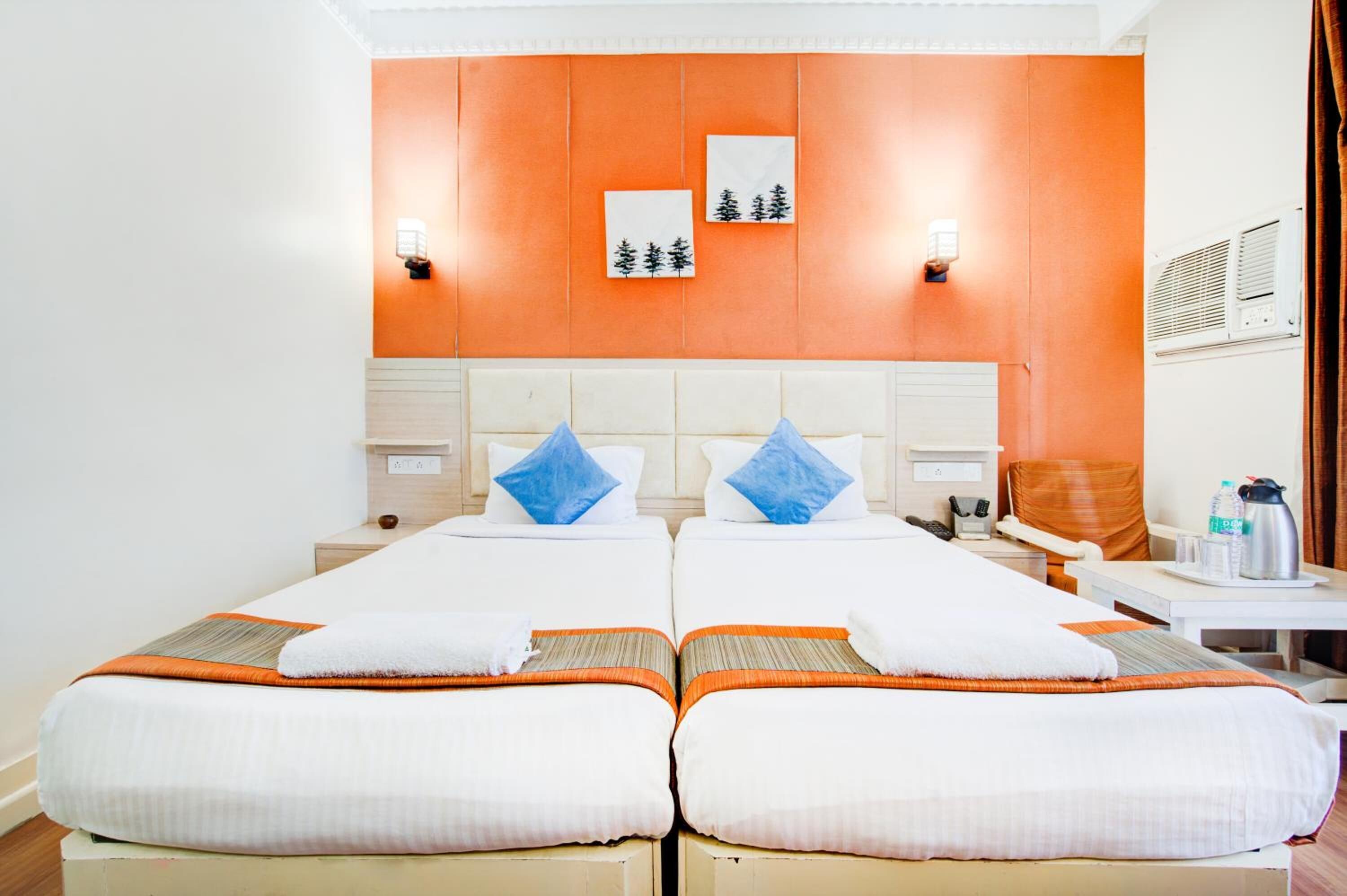 A double room with two beds, each with white linens and blue pillows, a wooden headboard, and a small table with a kettle and cups.