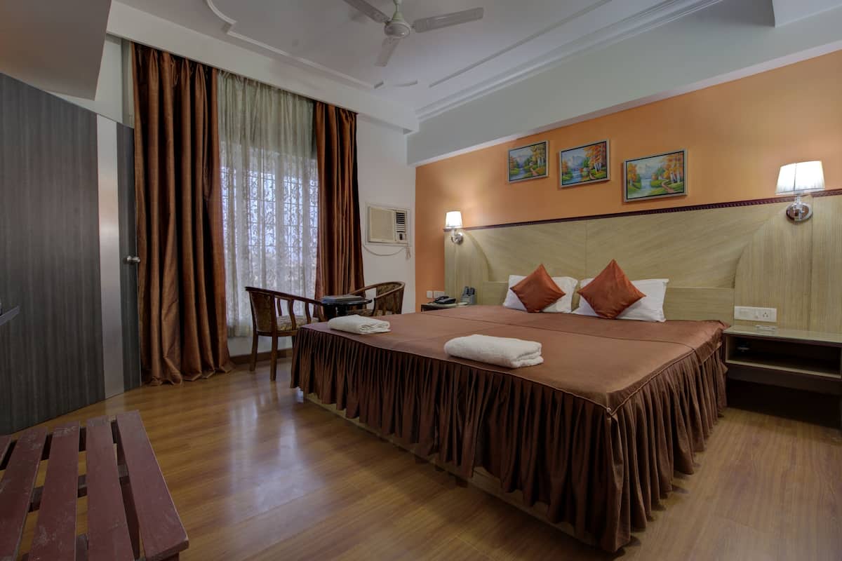 Quarto de hotel com uma cama grande, escrivaninha, cadeira e ventoinha no teto.