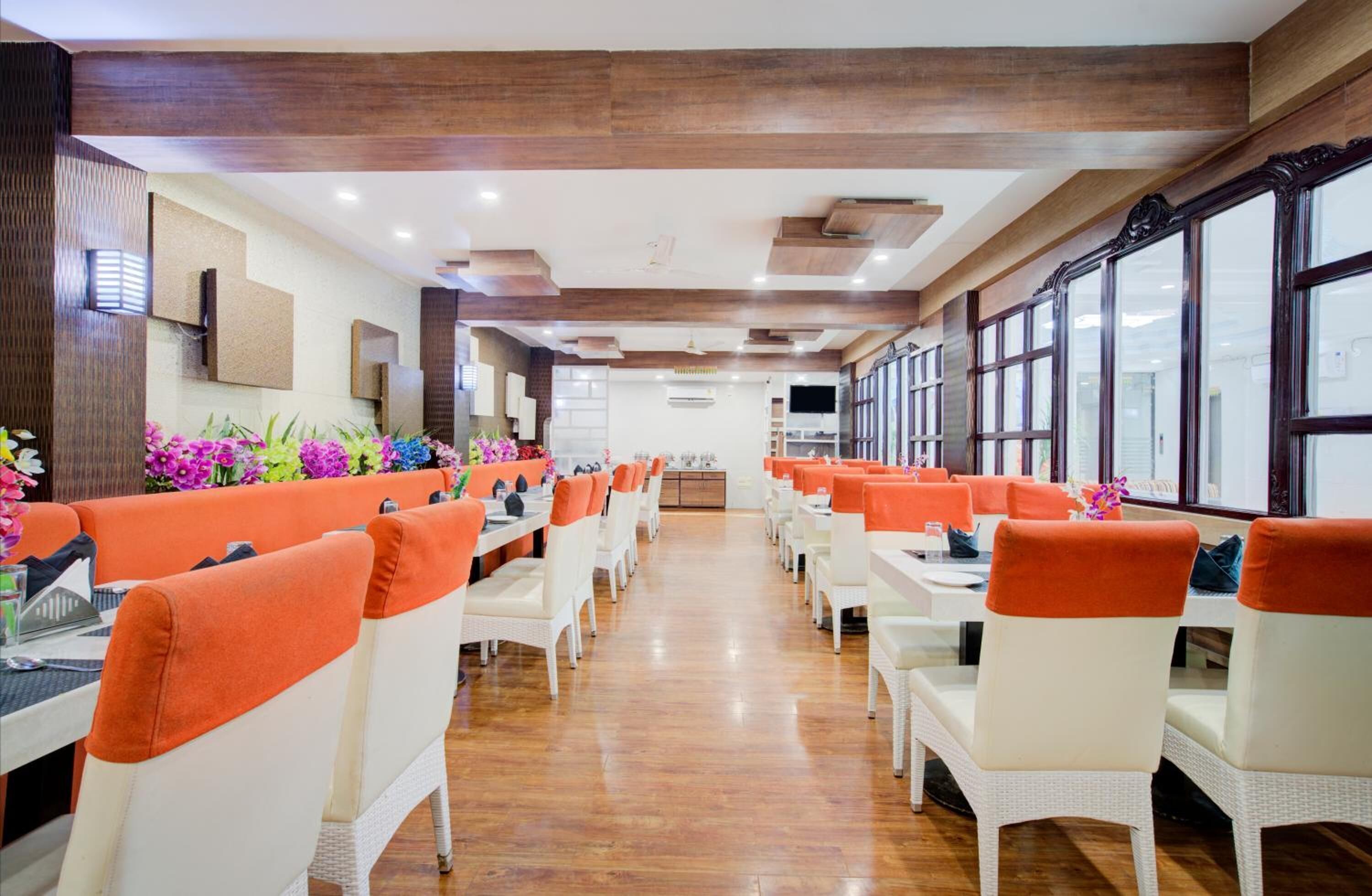 A restaurant with white wicker chairs and orange cushions, wooden floors, and large windows.