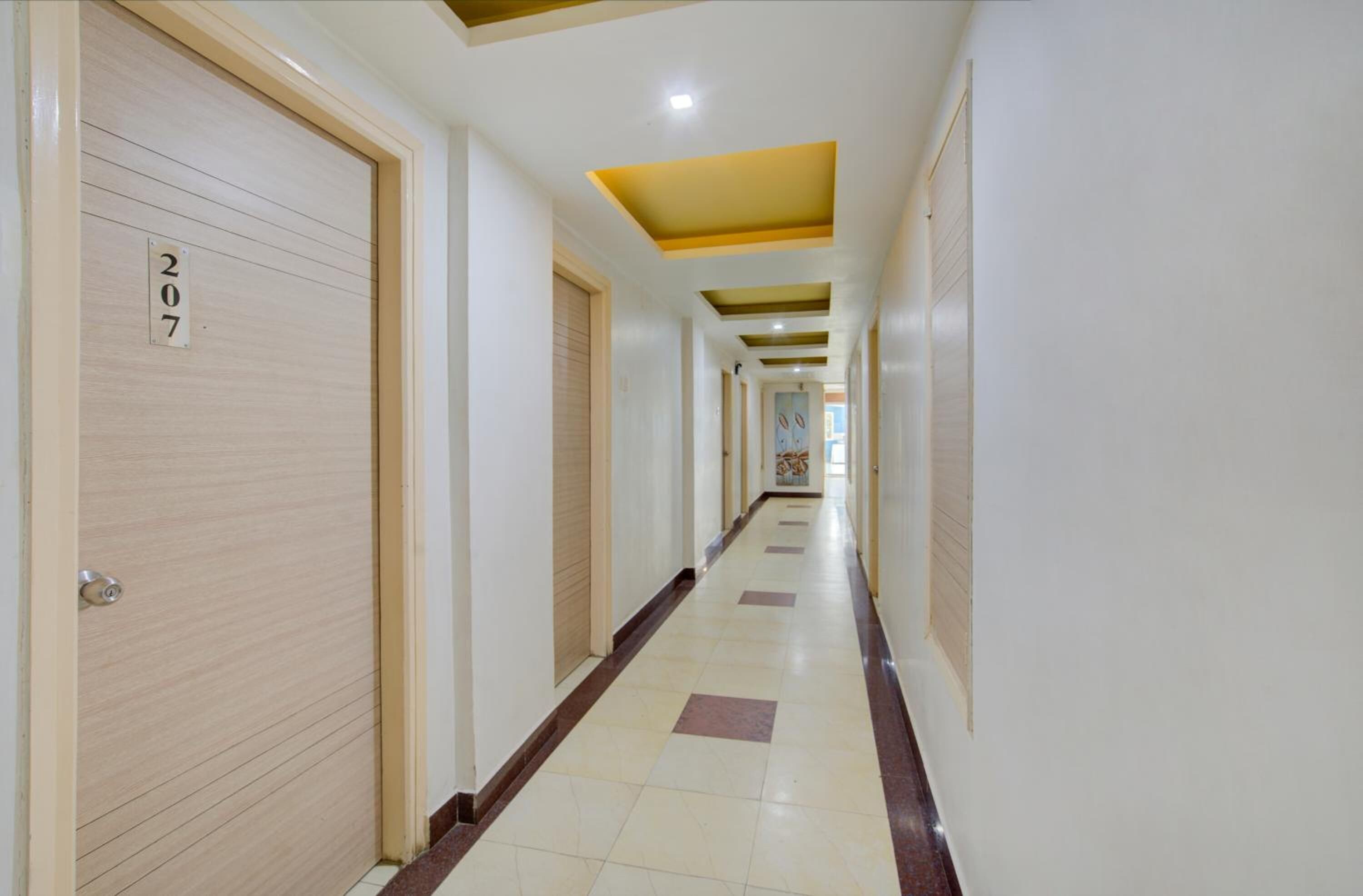 Pasillo de hotel con una puerta de madera que indica “207”, suelo de baldosas e iluminación empotrada en el techo.
