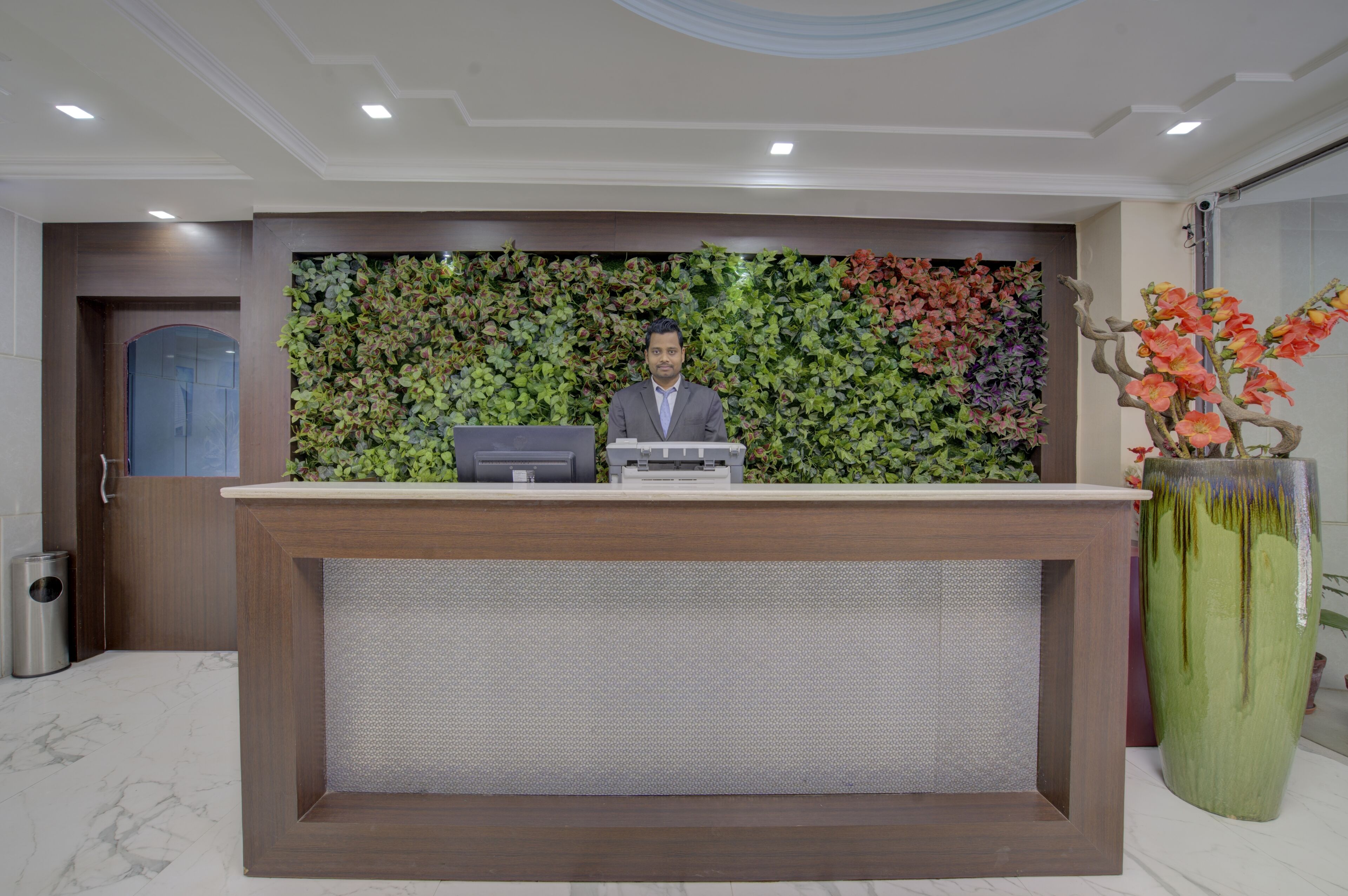A reception desk with a modern design, a digital printer, and a decorative plant wall behind.