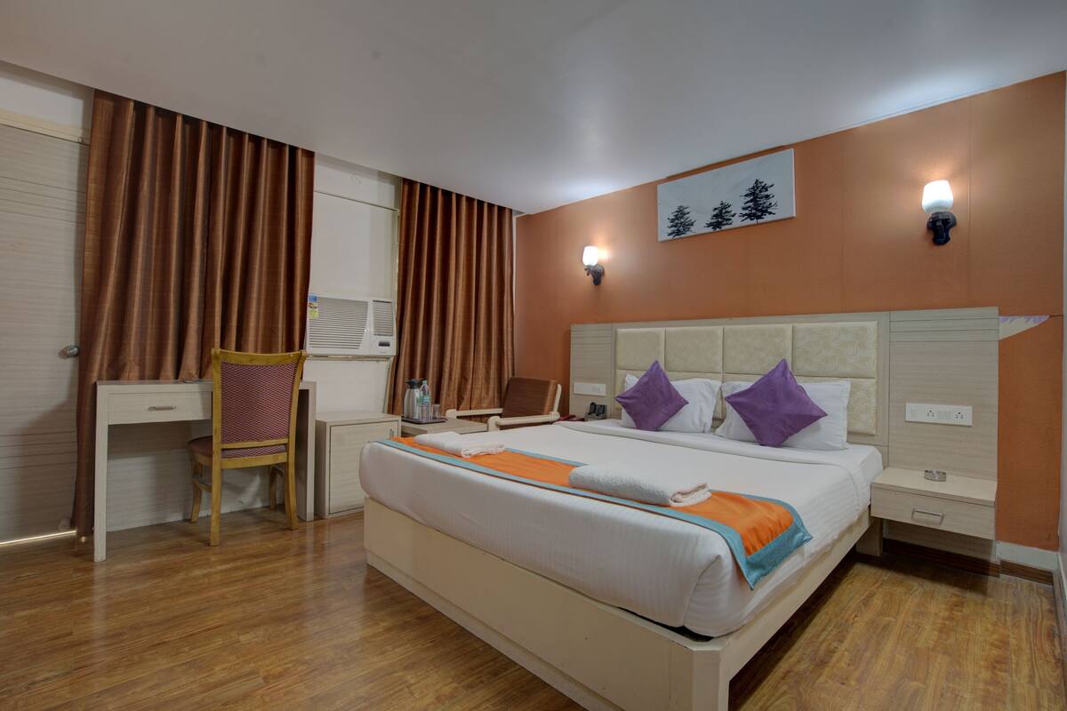Quarto de hotel com cama, escrivaninha, cadeira e um quadro na parede.