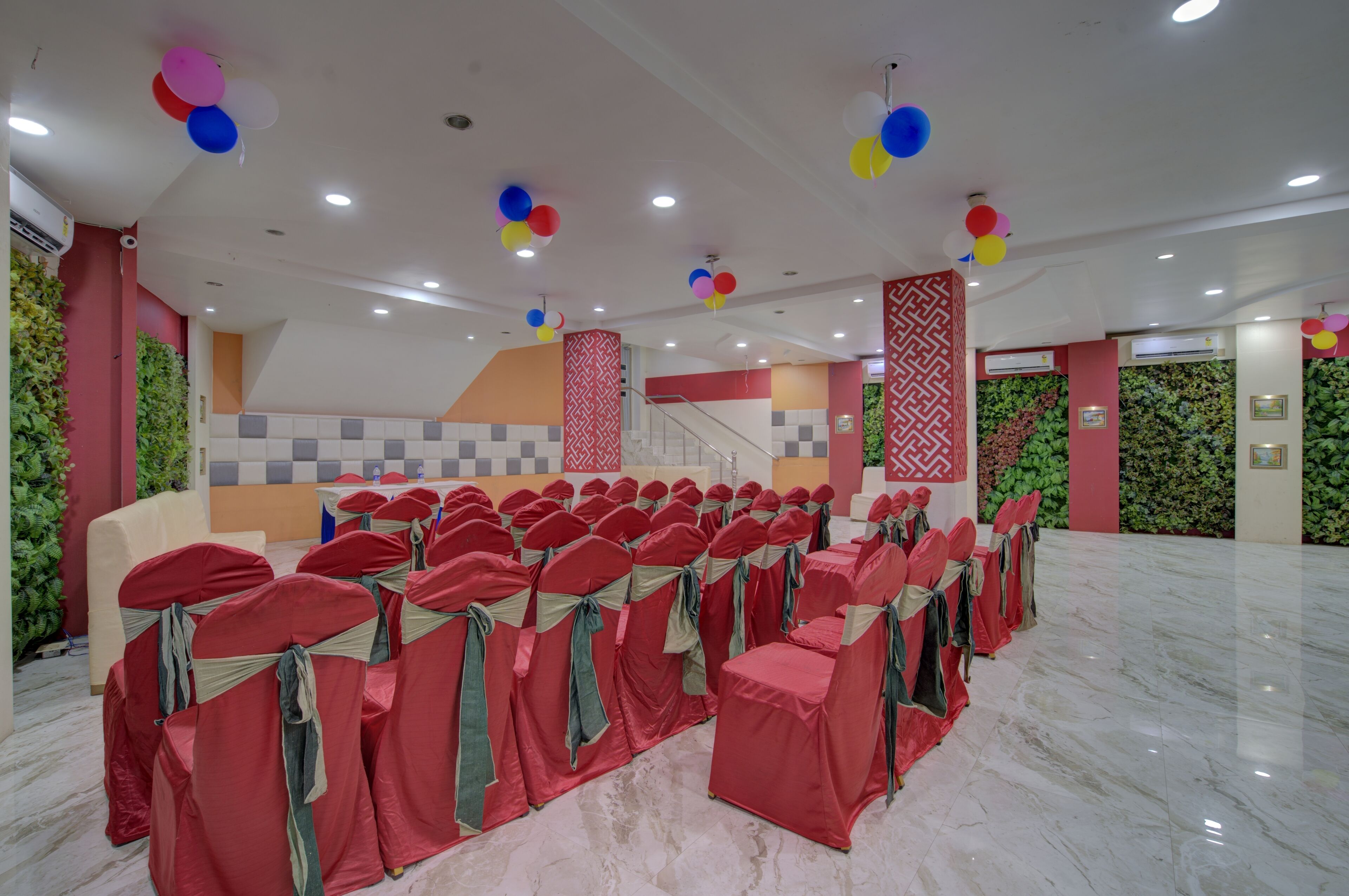 Un salón amplio con filas de sillas tapizadas de rojo, una escalera y paneles decorativos en las paredes.