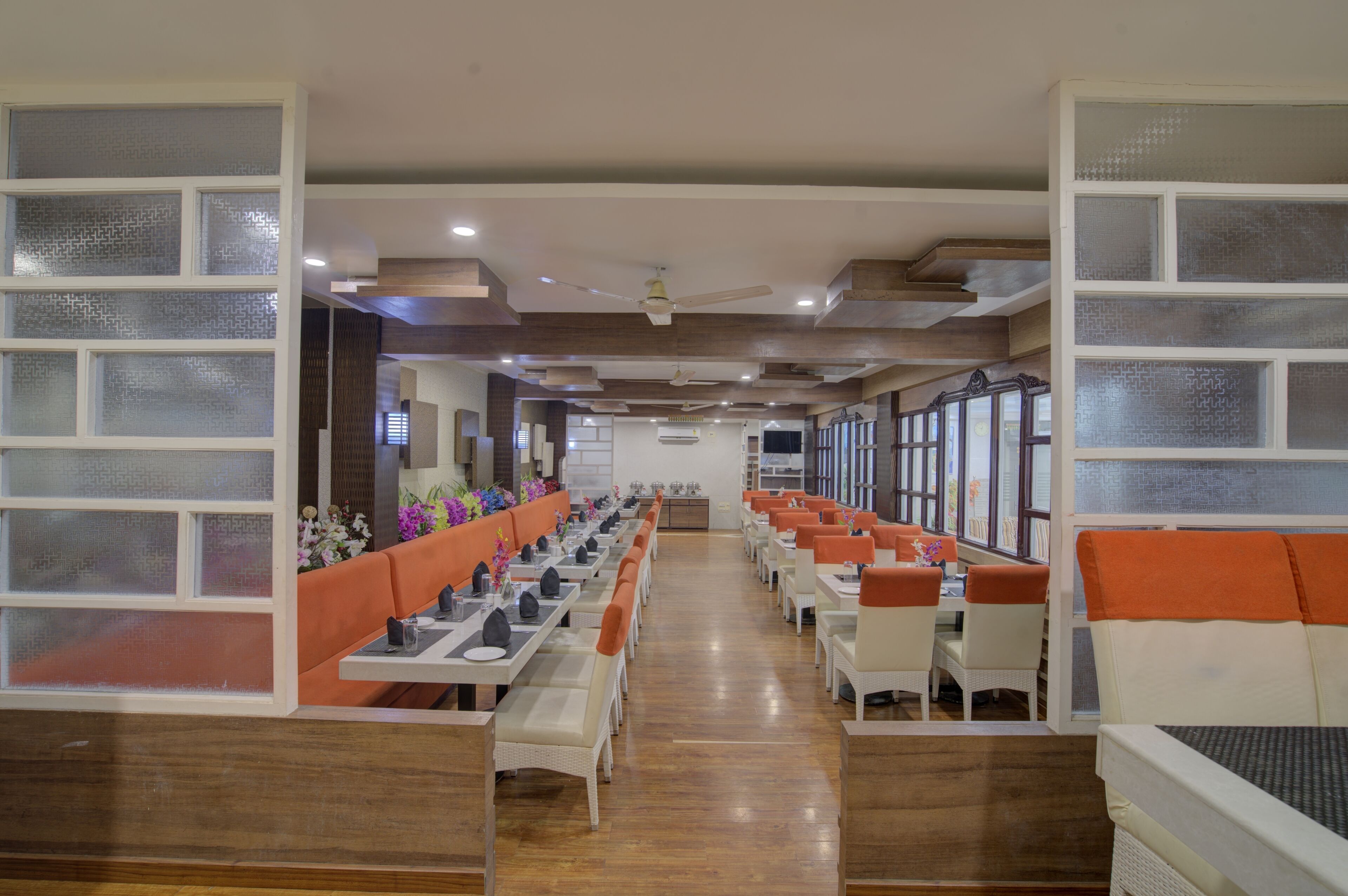 A restaurant with long communal tables, orange cushioned booths, and a wooden floor.