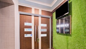 A hotel entrance with a wooden double door, a green artificial grass wall, and a mounted television. - Hotel Mahadev Palace (Deoghar)