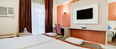 Habitación de hotel con dos camas, televisión, escritorio y ventana con cortinas.