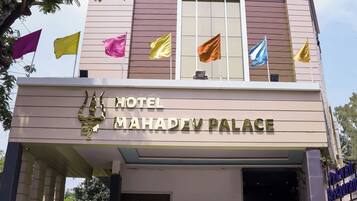 Un hotel moderno con una entrada destacada, varias banderas y un cartel que dice 'Hotel Mahadev Palace'.